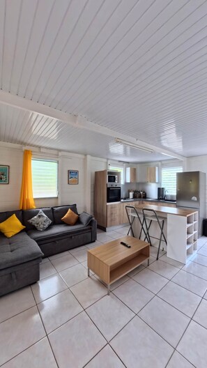 Una sala de estar moderna con sofá, mesa de centro y una cocina equipada con refrigerador, microondas y estufa.
