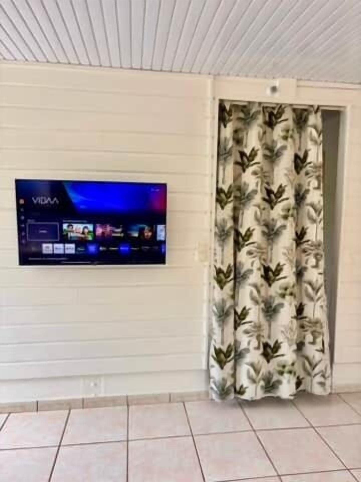 Una habitación con televisor de pantalla plana montado en la pared, cortina estampada y suelo de baldosas.