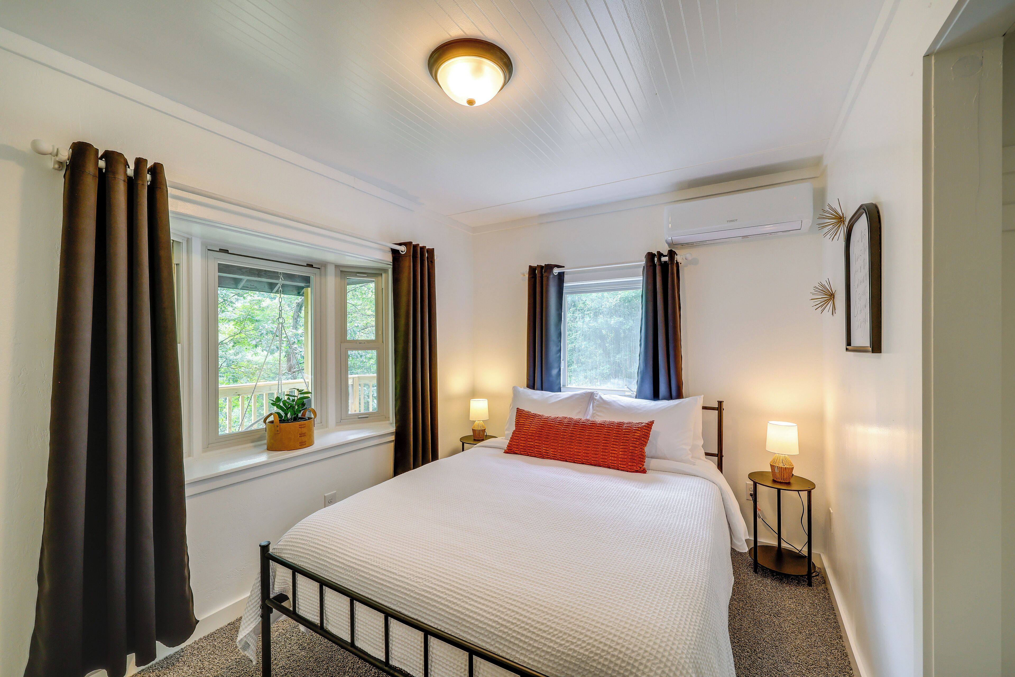 A neatly arranged bedroom with a bed, bedside lamps, a window with curtains, and a ceiling light fixture.
