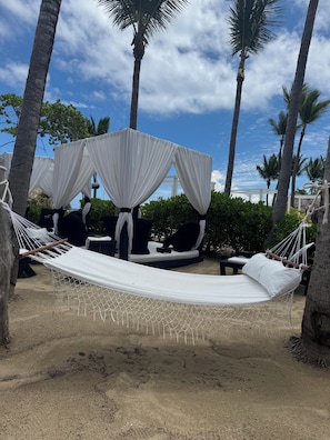 A hammock set up between two palm trees, with a white canopy overhead and a white mattress.