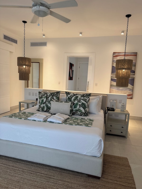 A modern bedroom with a large bed, two bedside tables, a ceiling fan, and a hanging light fixture.