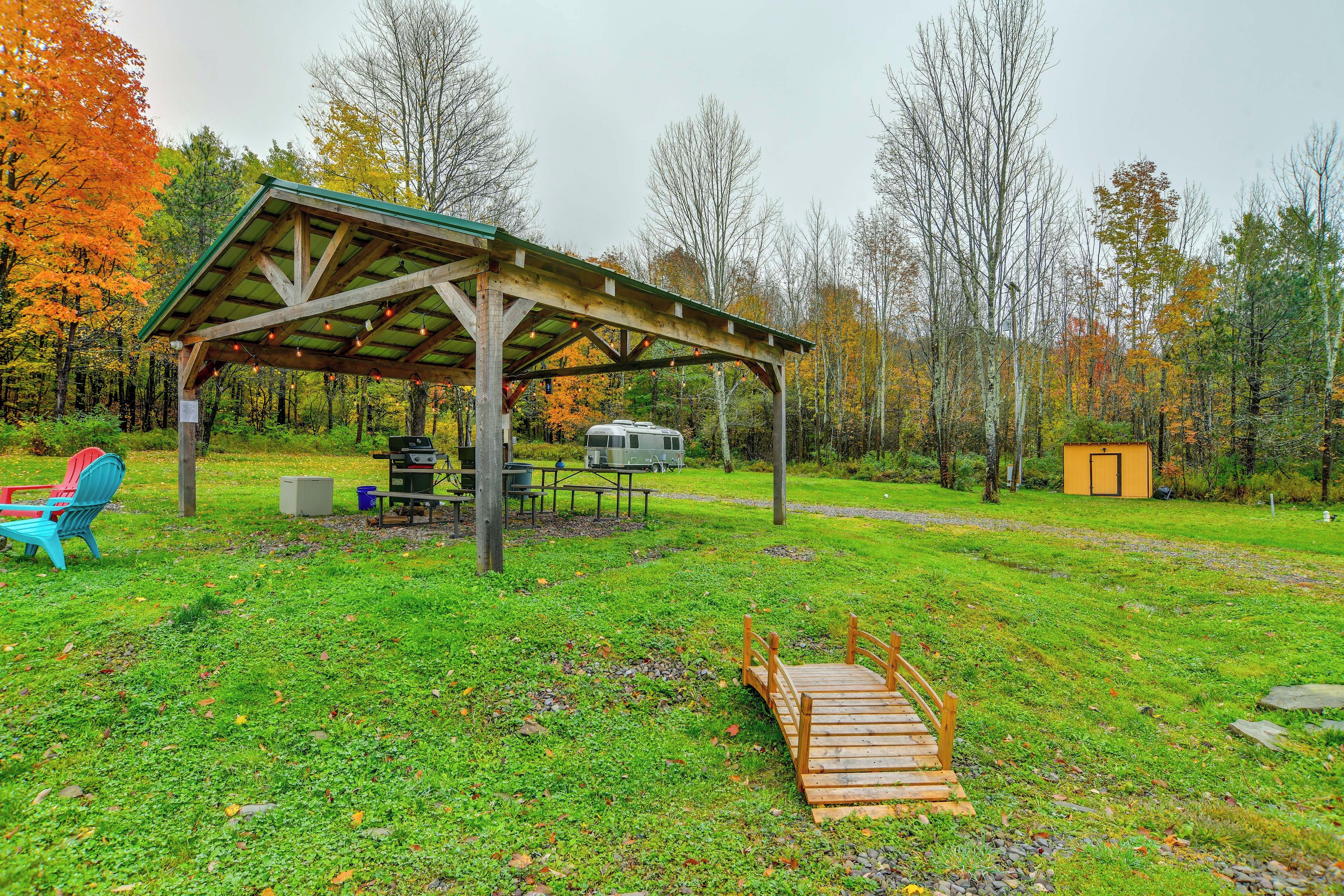 A covered picnic area with a grill, seating, and a portable toilet.