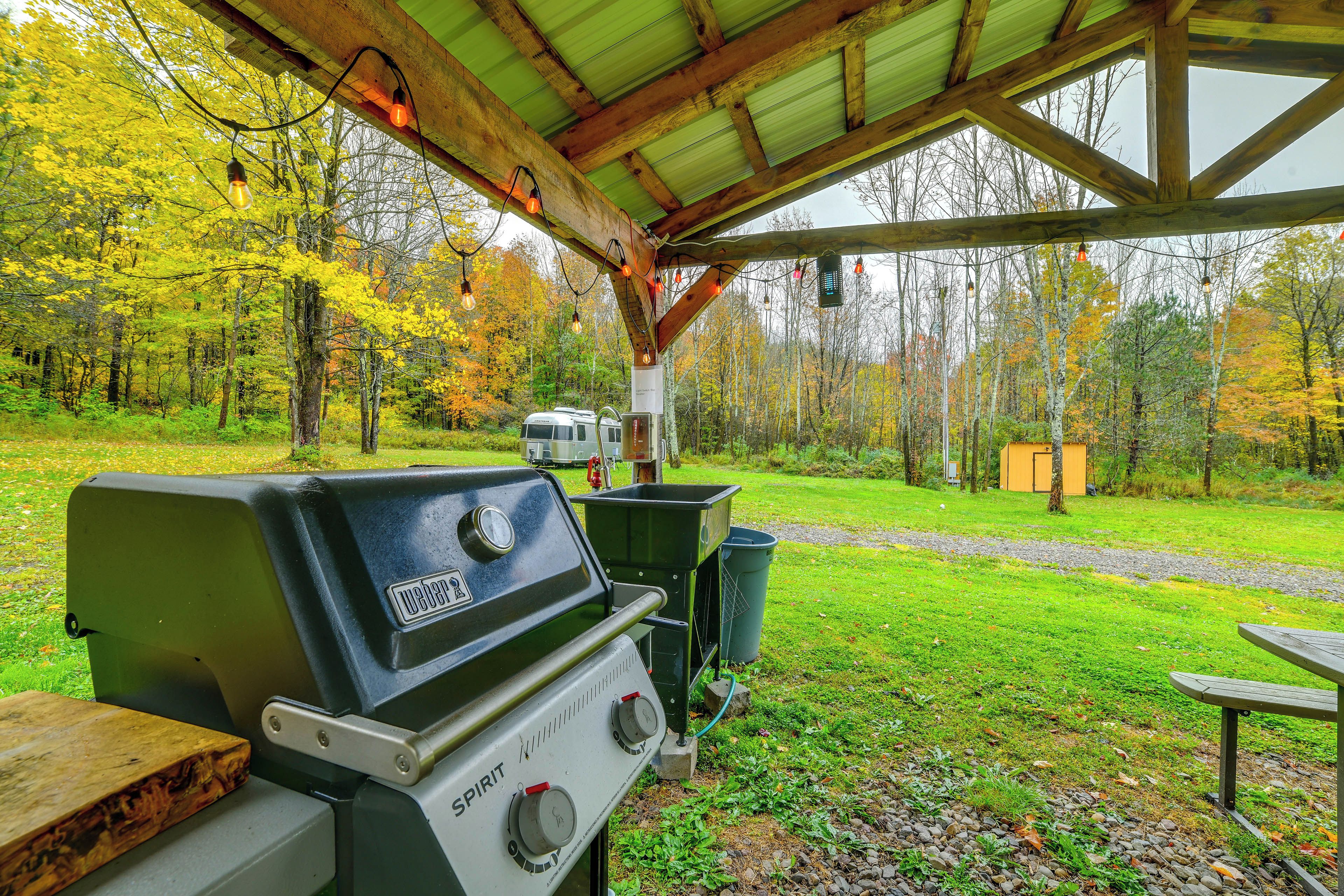 An outdoor grill area with a covered pavilion, a trash bin, and a picnic table.