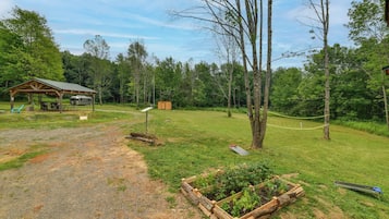 A campsite with a covered picnic area, a small shed, and a dirt path leading through a grassy field.