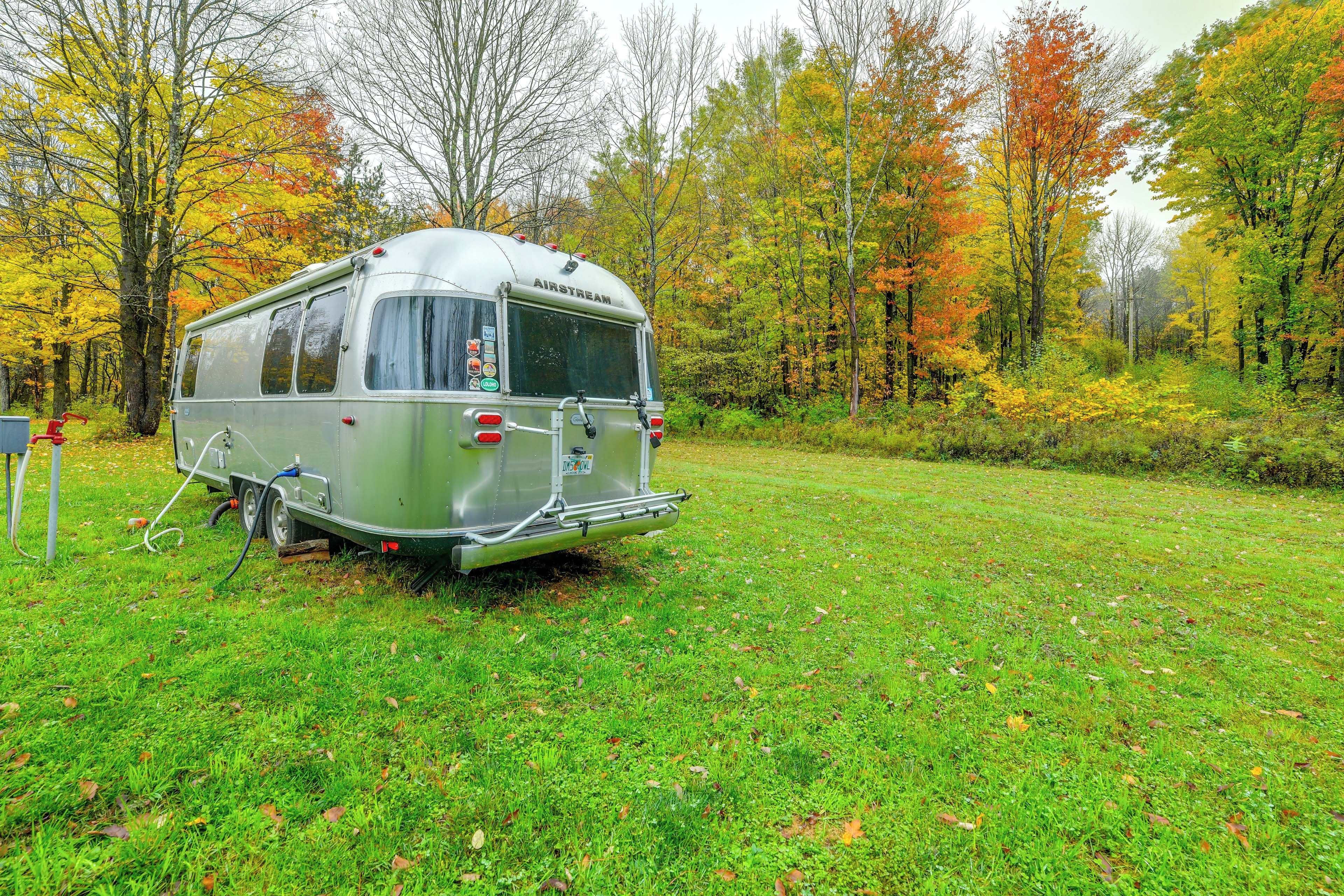 A stationary trailer with a flatbed, parked on grass with trees in the background.