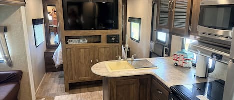 A compact RV kitchen with a stove, sink, and a large TV.