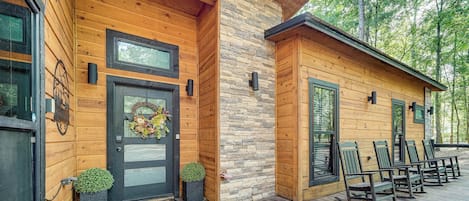 Een houten chalet met een gevel van steen, een voordeur met een krans, en een terras met stoelen.