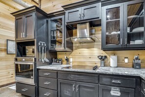 Une cuisine moderne avec des meubles de couleur sombre, une hotte en acier inoxydable et un plan de travail en granit.