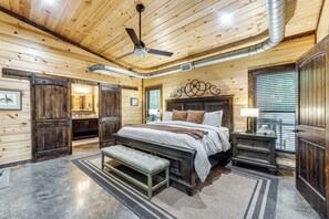 A log cabin bedroom with a bed, bench, bedside table, and a ceiling fan. - Hike, Soak & Play! Luxe Broken Bow Escape (Broken Bow)