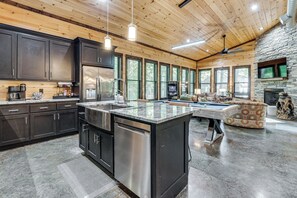 A spacious kitchen with a central island, dark cabinetry, and a stone fireplace. - Hike, Soak & Play! Luxe Broken Bow Escape (Broken Bow)