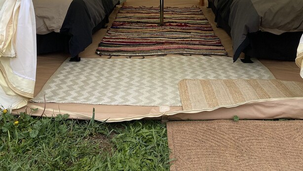A tent with two beds, a central pole, and a patterned rug.