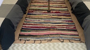 A tent with a bed, a bench, and a colorful woven rug.