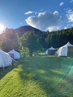 Yurts arranged in a grassy field with a forested mountain in the background.