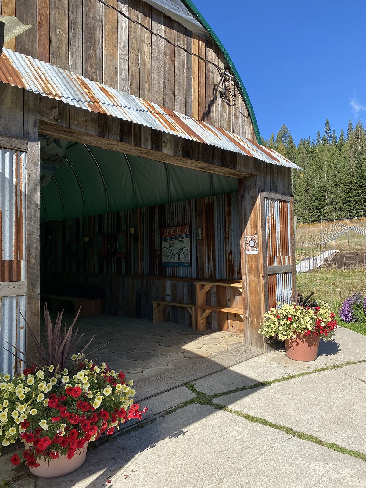 A rustic wooden building with a corrugated metal roof, a covered entrance, and a sign that reads 'Life is a bicycle ride.'