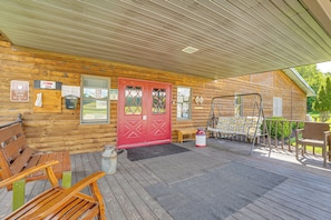 A wooden cabin with a red door, a porch with wooden benches, a swing set, and a clear view of the surrounding landscape.