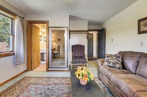 A living room with a sofa, a coffee table with a floral arrangement, a patterned rug, and a view of a dining area through an open door.