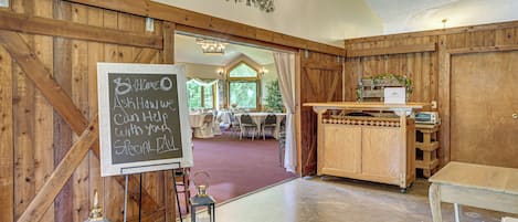 A rustic interior with a chalkboard sign, wooden walls, and a view into a dining area.