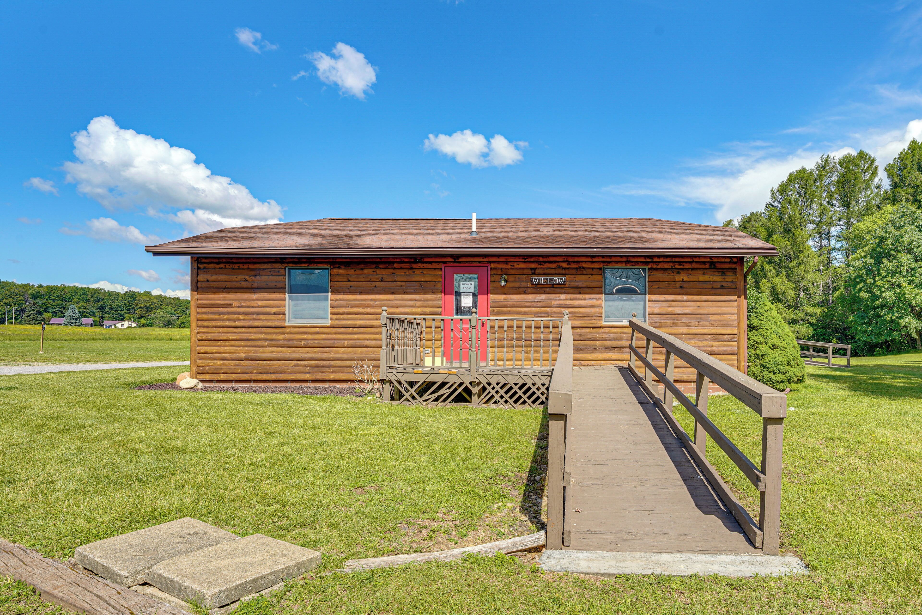 A wooden cabin with a red door, a small porch, and a wooden walkway leading to the entrance.