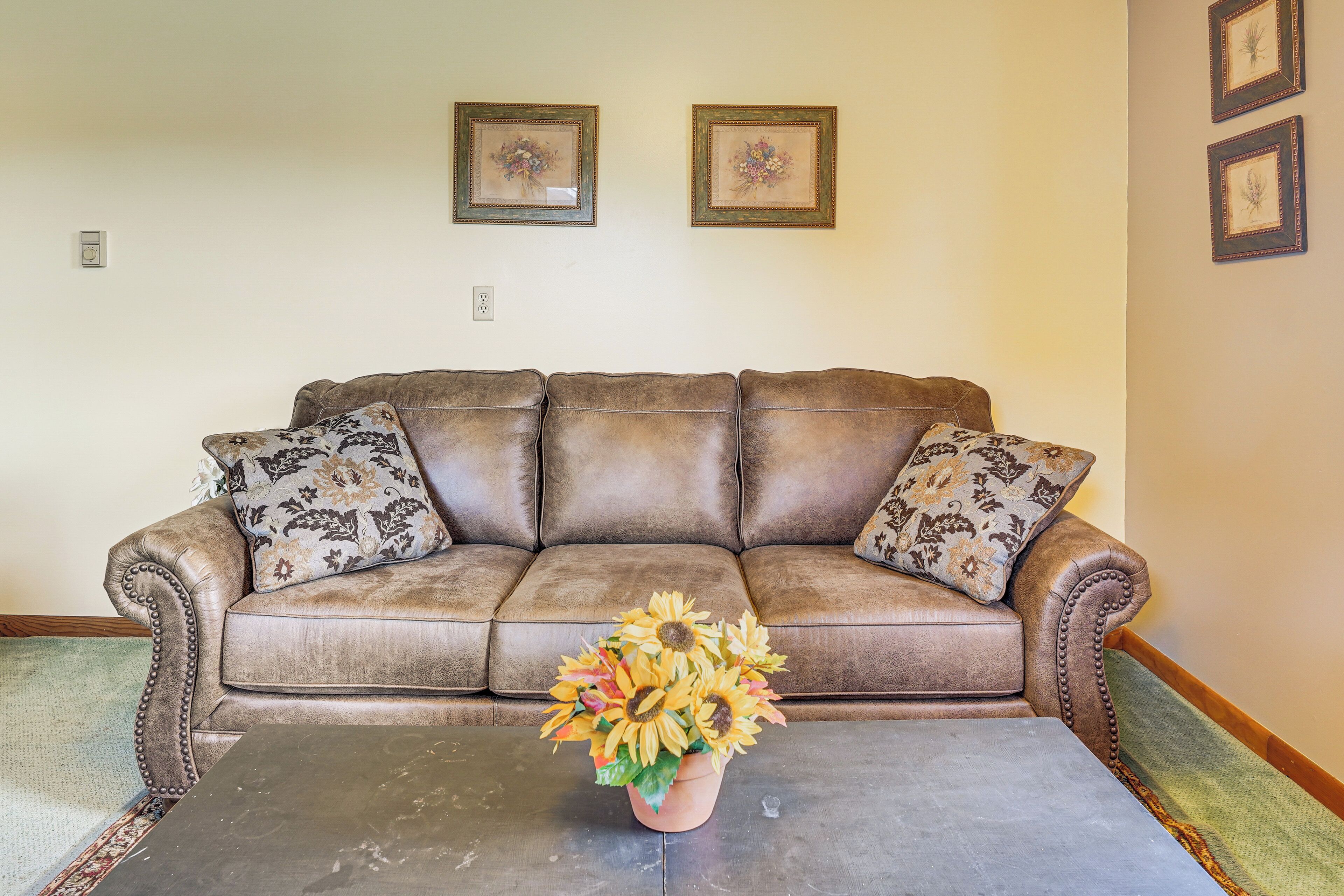 A brown leather sofa with patterned cushions, a coffee table, and a floral arrangement.