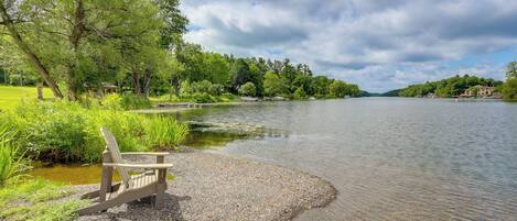 Une vue sur le lac, avec une chaise en bois placée sur un chemin de gravier, le tout entouré d’une végétation luxuriante et d’arbres.