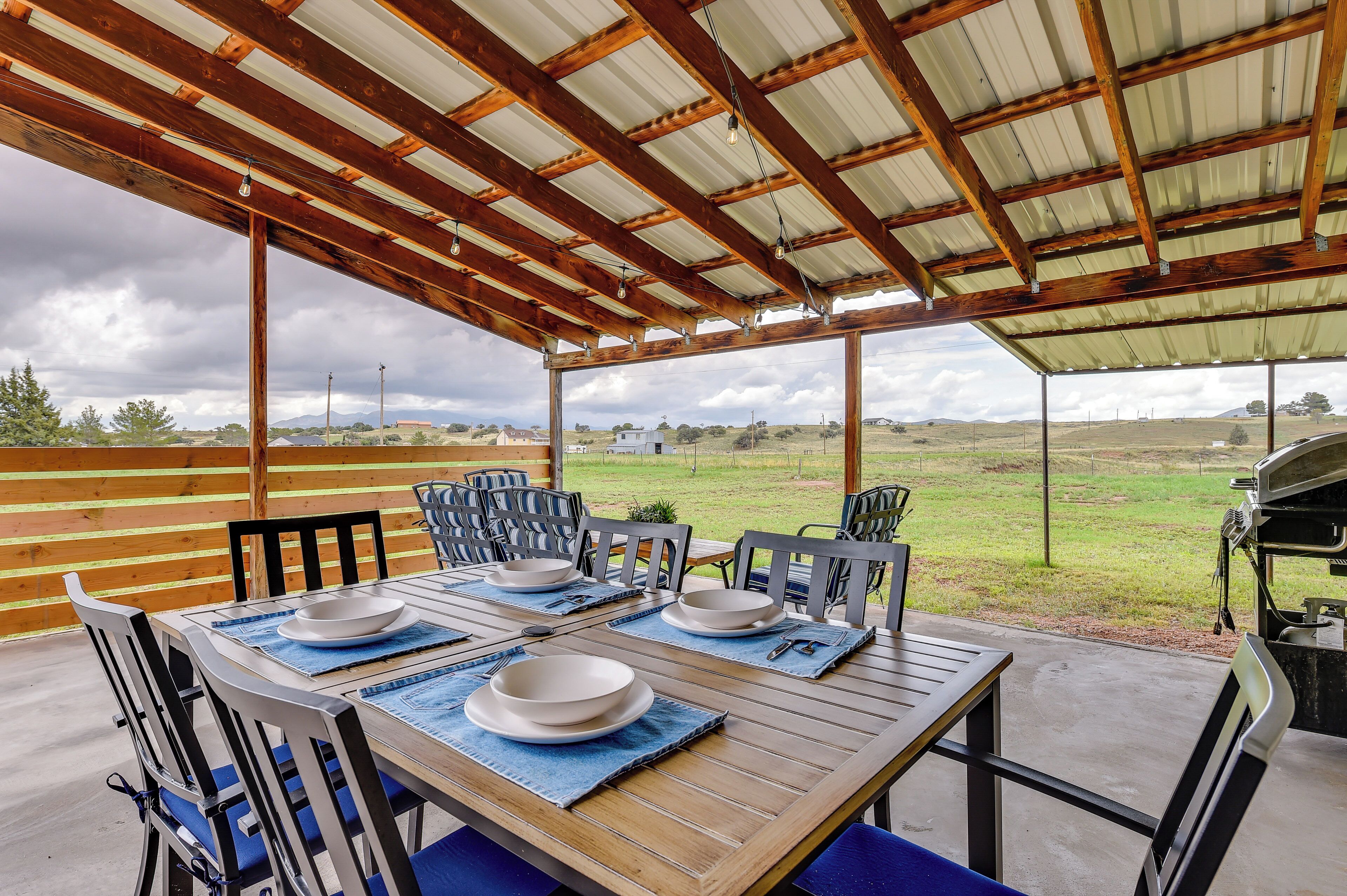 Une terrasse extérieure couverte, aménagée avec une table pour les repas, des chaises et un barbecue.