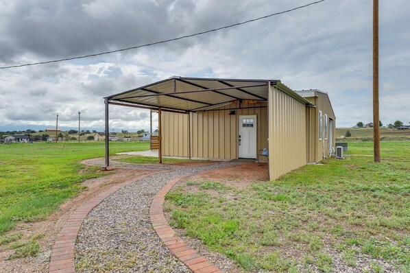 A small, single-story building with a metal roof and a door, surrounded by a gravel path and grass. - Tranquil Wine Country Getaway w/ Hillside Views (Elgin)