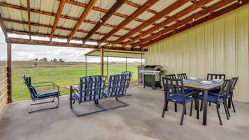 Un patio al aire libre con mesa y sillas, una parrilla y vistas al campo.