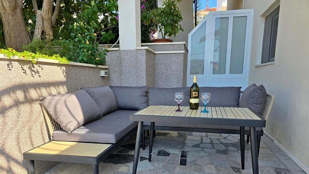 Ein Sitzbereich im Freien mit Tisch und Stühlen, einer Weinflasche und einem Glas.