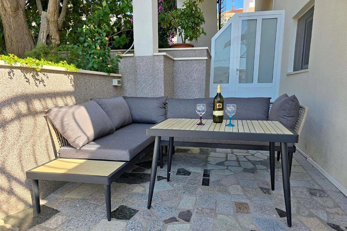 An outdoor seating area with a table and chairs, a bottle of wine, and a glass.
