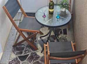 A small outdoor seating area with a round glass table, two wooden chairs, a bottle of wine, and a glass. - Lux Adriatica Apartments (Okrug)