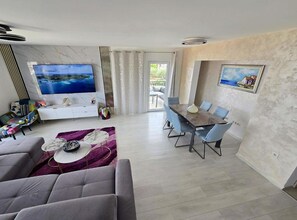 A modern living room with a grey sofa, a coffee table, and a TV mounted on the wall. - Lux Adriatica Apartments (Okrug)