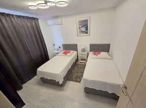 A hotel room with two single beds, a nightstand, a lamp, a painting on the wall, and a window with curtains. - Lux Adriatica Apartments (Okrug)