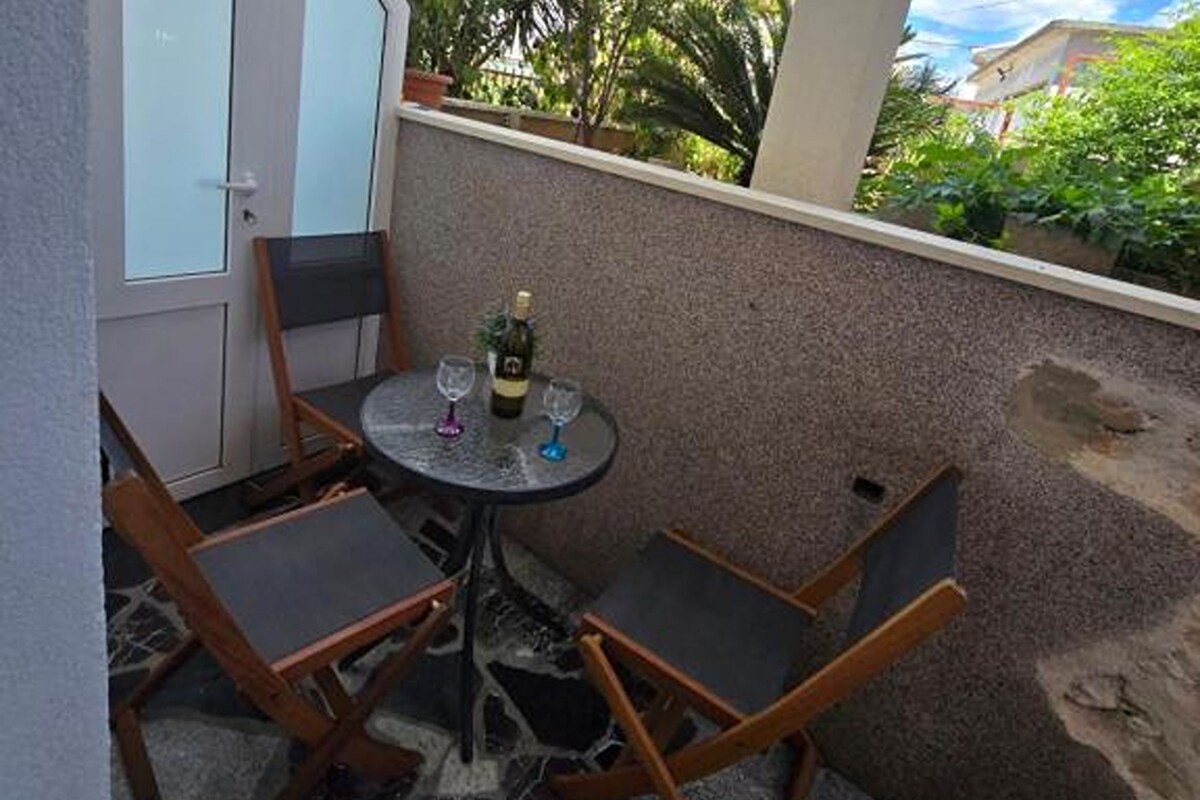 A small outdoor seating area with a round table and four chairs, a bottle of wine, and two wine glasses.