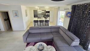 Ein modernes Wohnzimmer mit einem grauen Ecksofa, einem Essbereich mit Barhocker und einer Küche im Hintergrund.