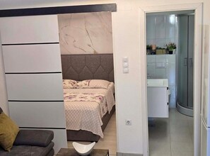 Ein Schlafzimmer mit einem Bett, einem grauen Kopfteil, einem Nachttisch und einem Sofa.