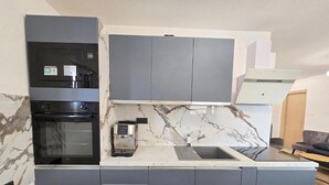 Eine moderne Küche mit grauen Schränken, einem Einbauofen, einer Kaffeemaschine und einer Marmor-Spritzschutzwand.