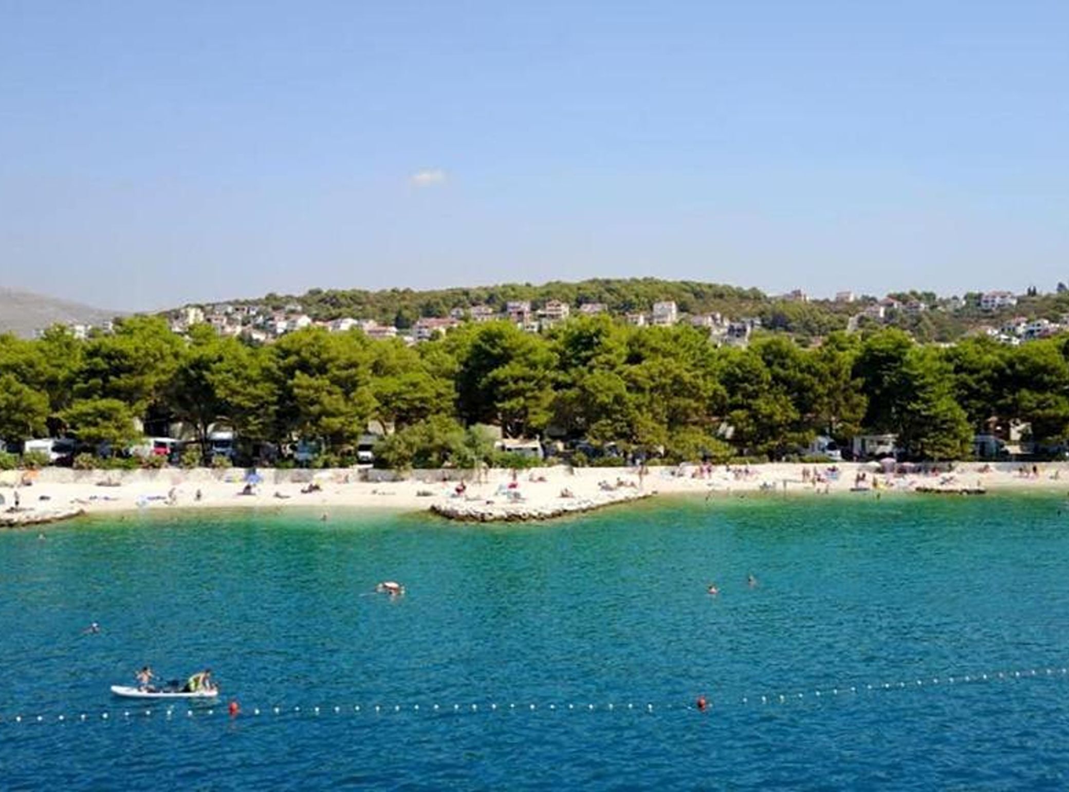 A coastal area with a beach, clear blue water, and a backdrop of residential buildings.