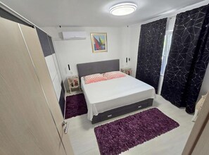 A bedroom with a bed, a nightstand, a dresser, a window with curtains, and a ceiling light. - Lux Adriatica Apartments (Okrug)
