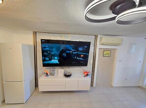 A living room with a flat-screen TV mounted on a white entertainment unit, a white refrigerator, and an air conditioning unit on the wall. - Lux Adriatica Apartments (Okrug)