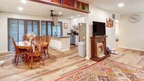 Un salón amplio con una mesa de comedor, sillas, una cocina al fondo, un televisor y un reloj decorativo en la pared.
