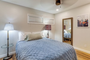 Quarto com cama, mesa de cabeceira, abajur, espelho e um quadro na parede.