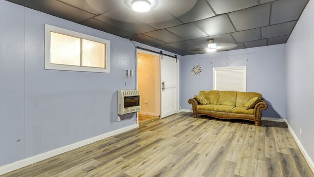 Una habitación con piso de madera, un sofá de estilo vintage, una lámpara de techo y una puerta que da a otra habitación.