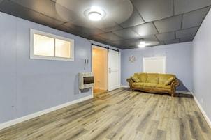 Una habitación con piso de madera, un sofá de estilo vintage, una lámpara de techo y una puerta que da a otra habitación.