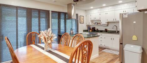 A modern kitchen with white cabinets, a stainless steel refrigerator, and a dining area with a wooden table and chairs.