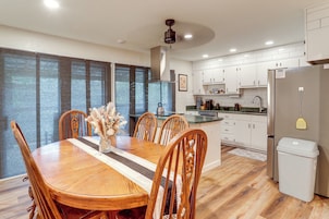 Una cocina moderna con armarios blancos, un refrigerador de acero inoxidable y una zona de comedor con mesa y sillas de madera.