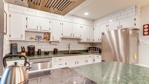 Una cocina moderna con armarios blancos, un refrigerador de acero inoxidable, un microondas y una tetera sobre la encimera.