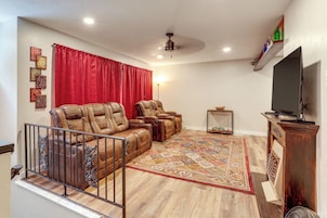 Una sala de estar con una cortina roja, un ventilador de techo, un televisor y un tapete estampado.