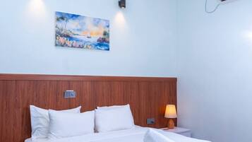 Habitación de hotel con cama, ventilador de techo, unidad de aire acondicionado y un cuadro en la pared.