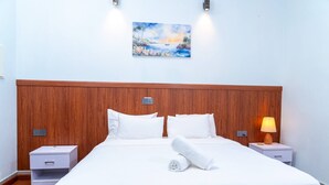 Et hotelværelse med sengegavl i træ, hvidt sengetøj, et billede på væggen og en senelampe.
