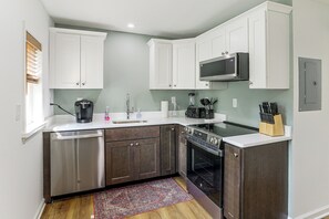 Una cocina funcional con armarios blancos, lavavajillas, estufa y microondas.